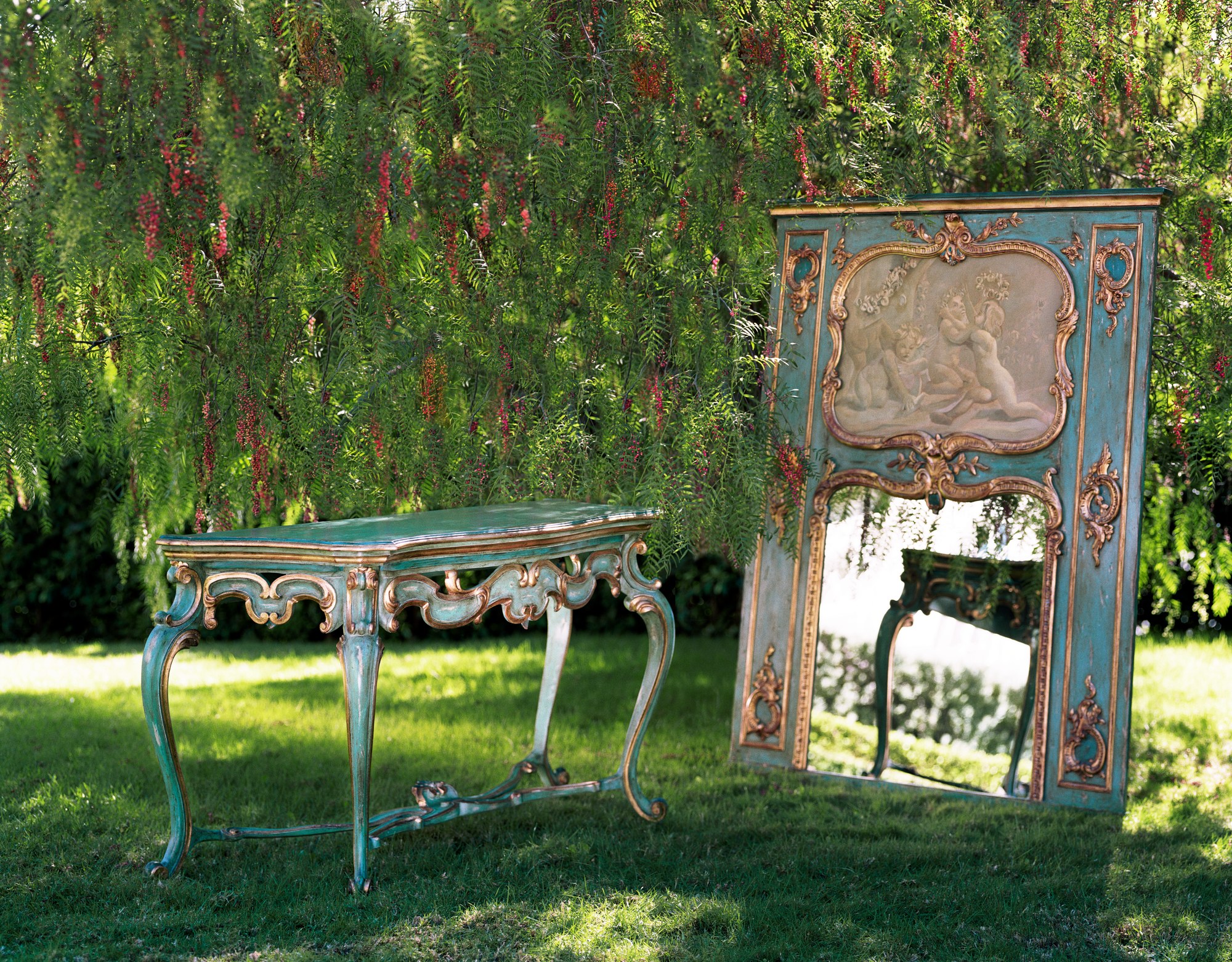 Allyson trumeau and console, painted blue-green with gilt carving and a mirror below a relief panel, photographed outdoors under a pepper tree