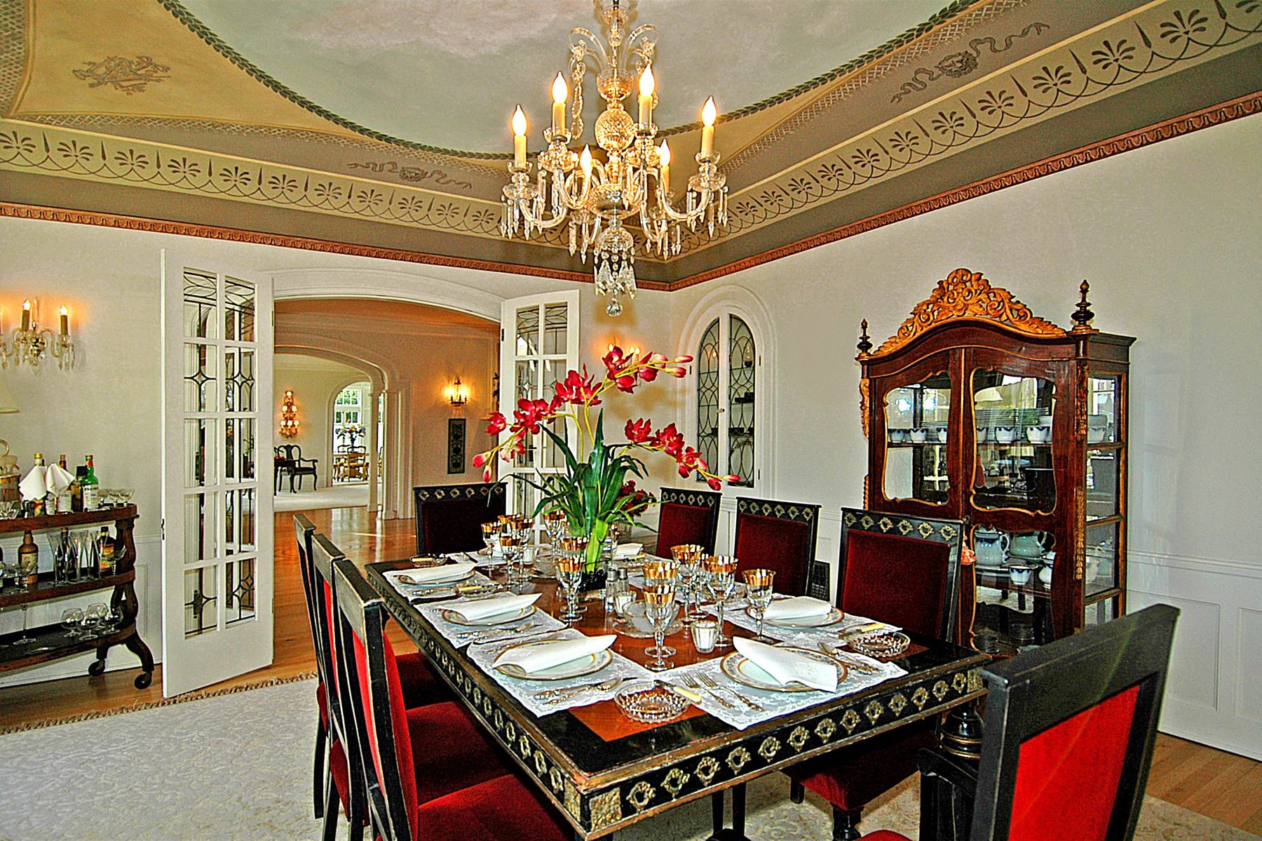 Dining room set for dinner beneath a crystal chandelier and a painted ceiling frieze