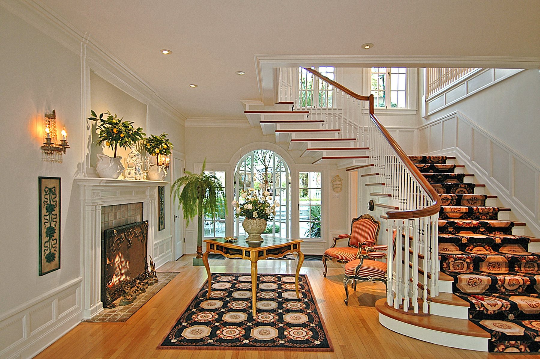 Entrance hall with a lit fireplace, a curved staircase and an arched garden window