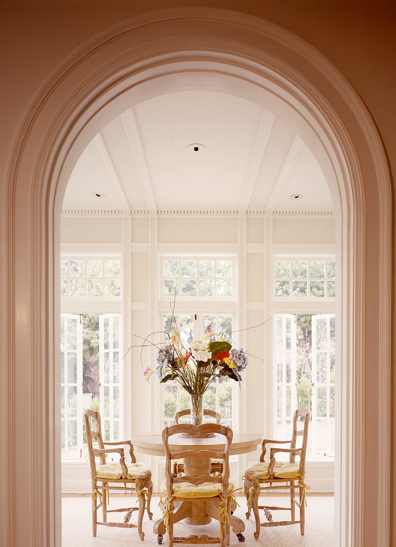 Garden room seen through an arched doorway, a round table set before tall windows