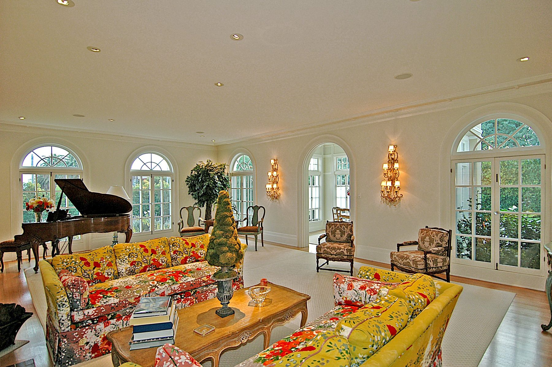 Living room with a grand piano, arched French windows and floral sofas