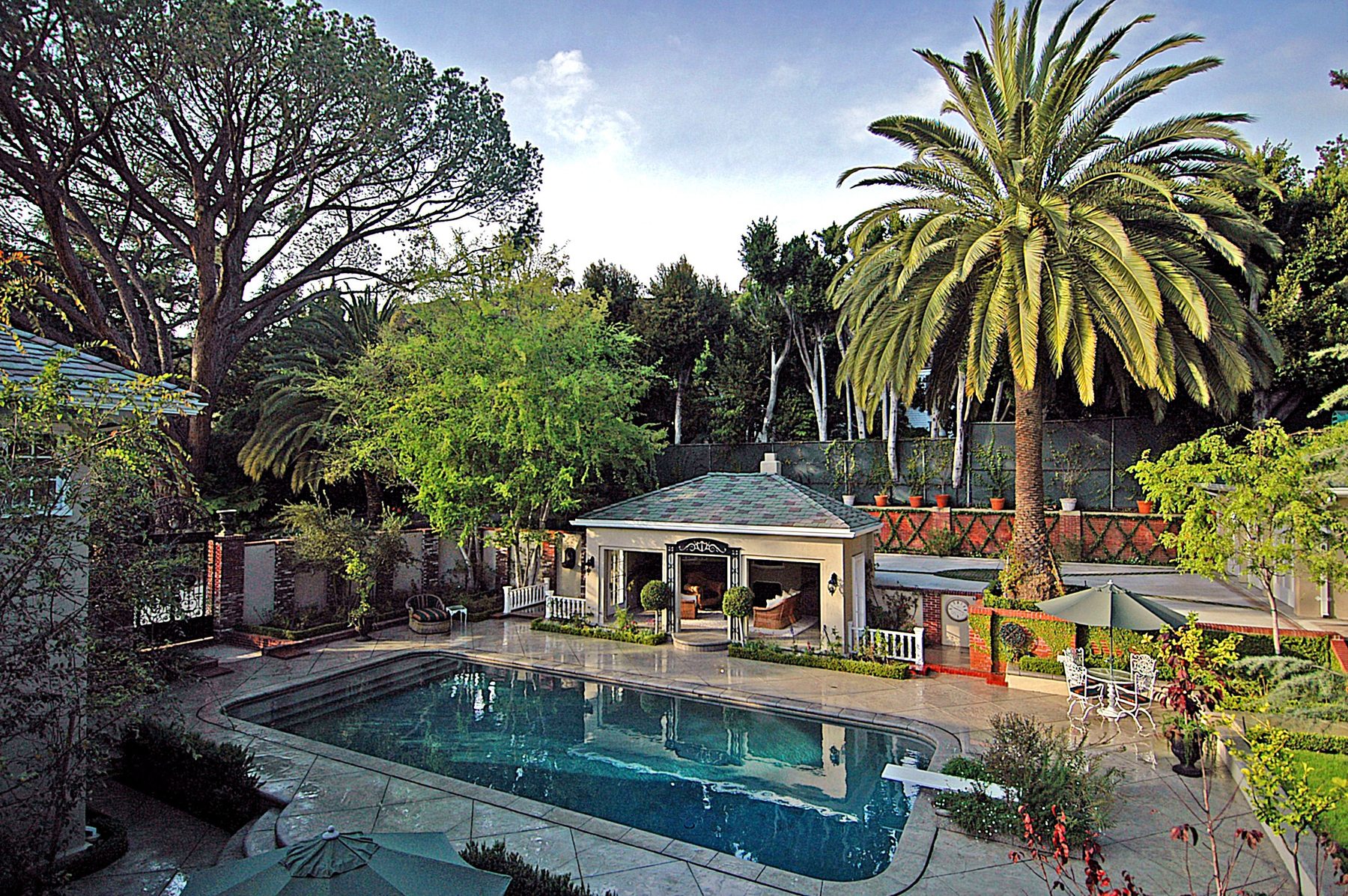 The yard and pool with the pool house beyond, under palms and pines