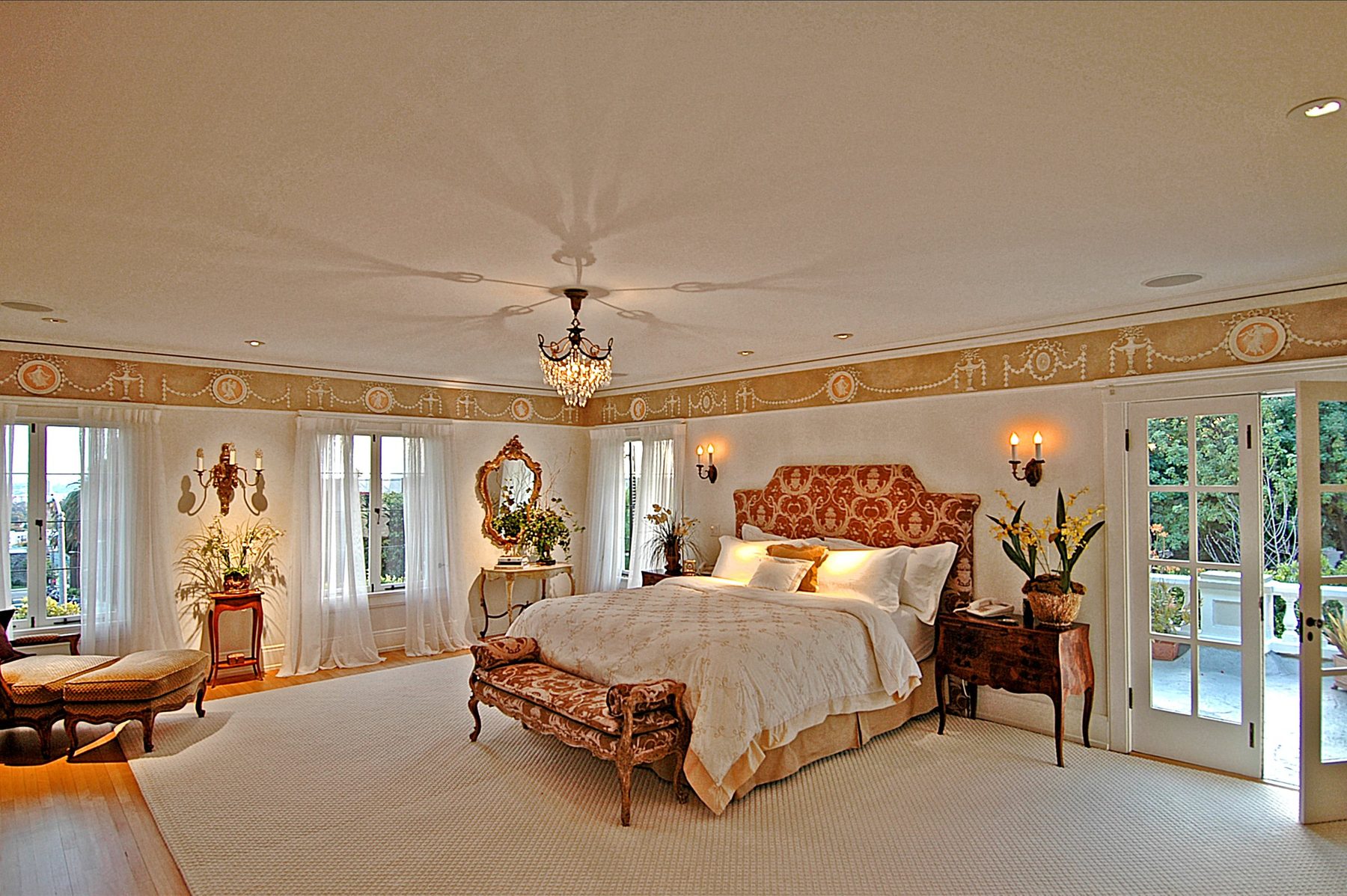 Principal bedroom with a painted frieze, a crystal chandelier and French doors to a balcony