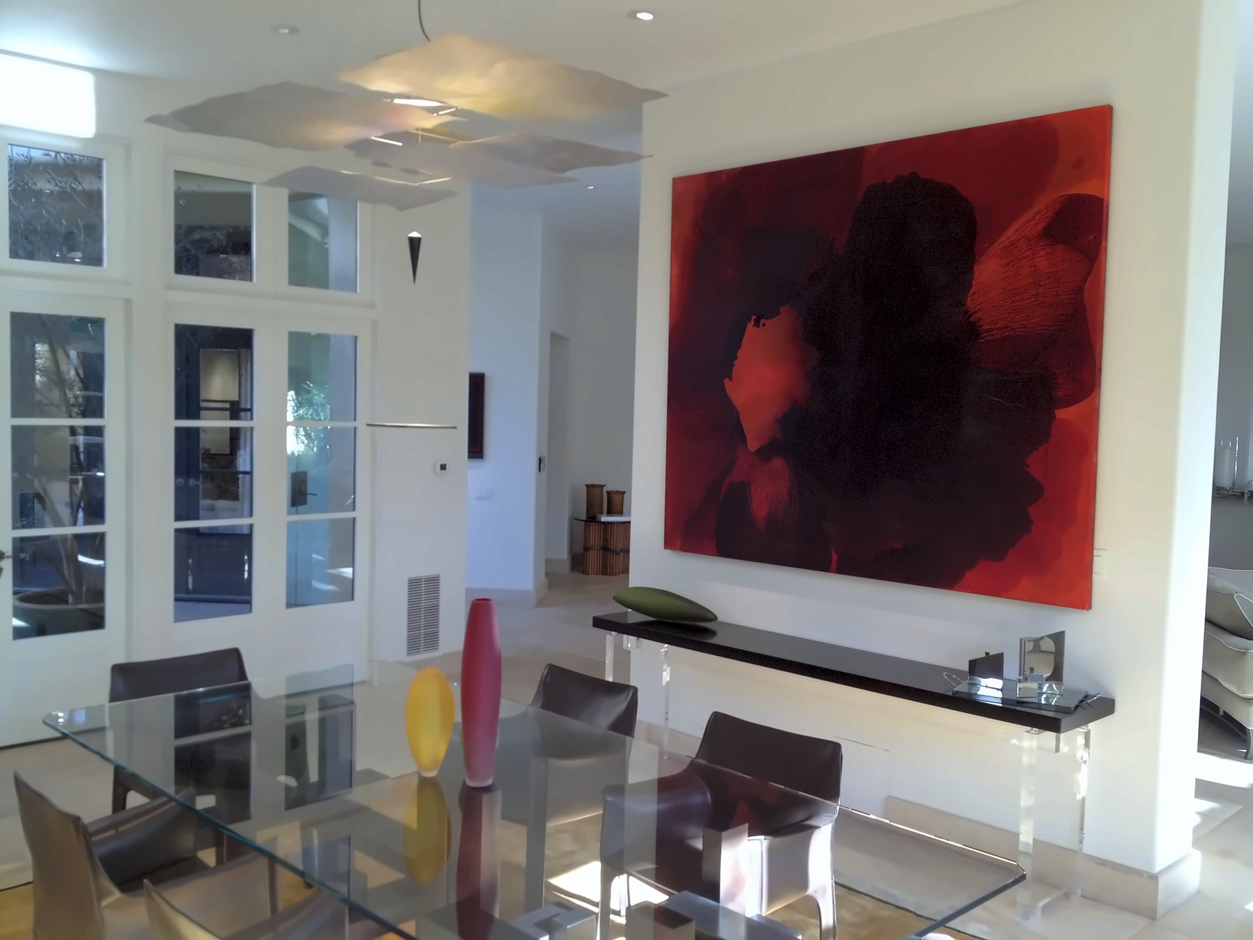 Dining room with a glass table, a long floating console and a large red painting