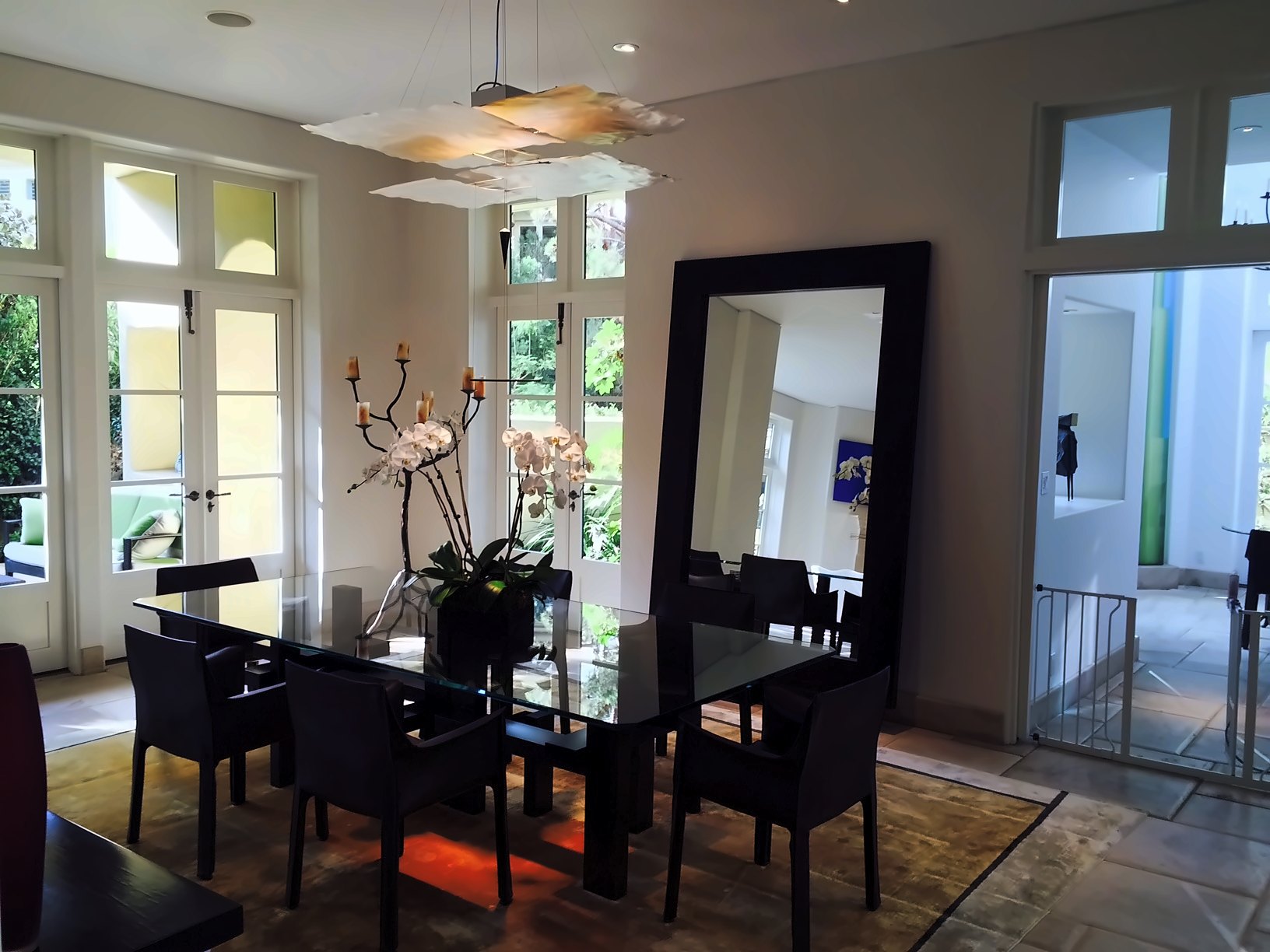 Dining room with black chairs, an orchid centerpiece, a tall framed floor mirror and French doors