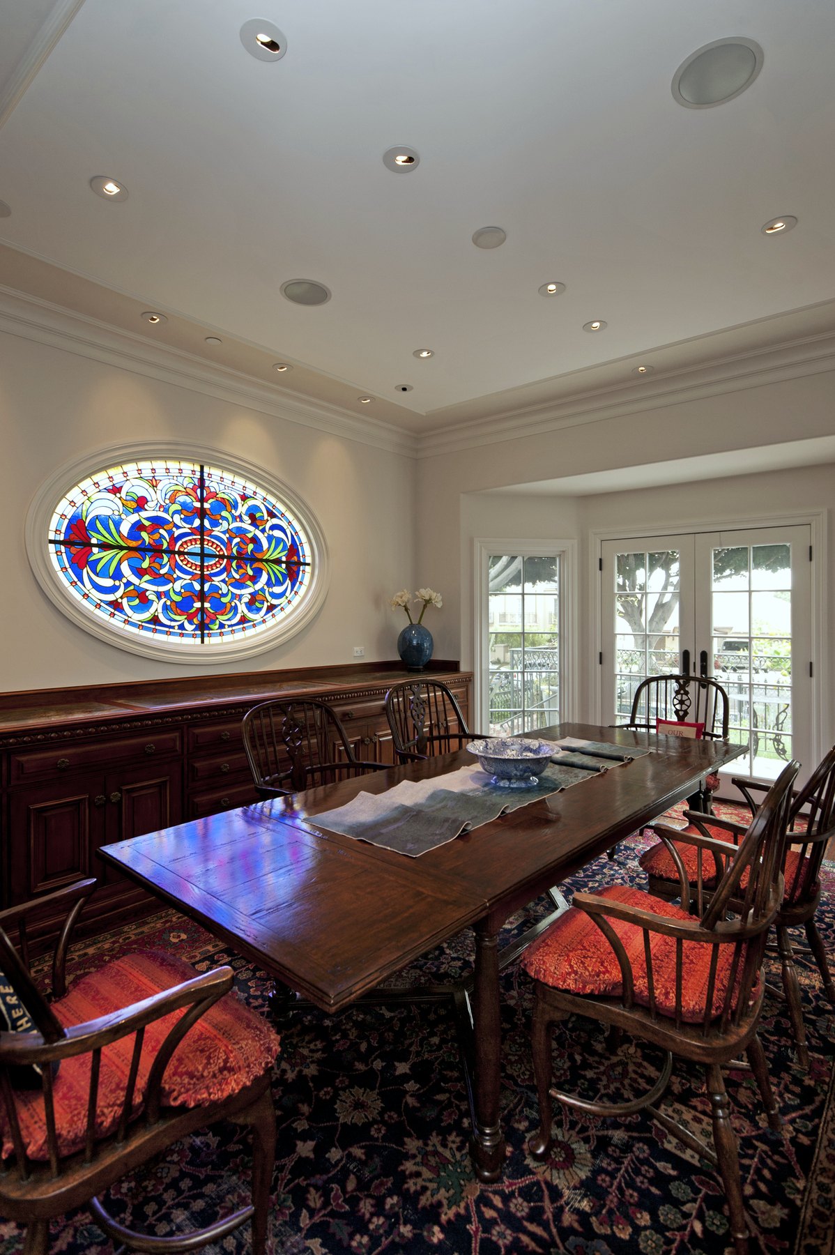 Dining room with red chairs beneath an oval stained-glass window