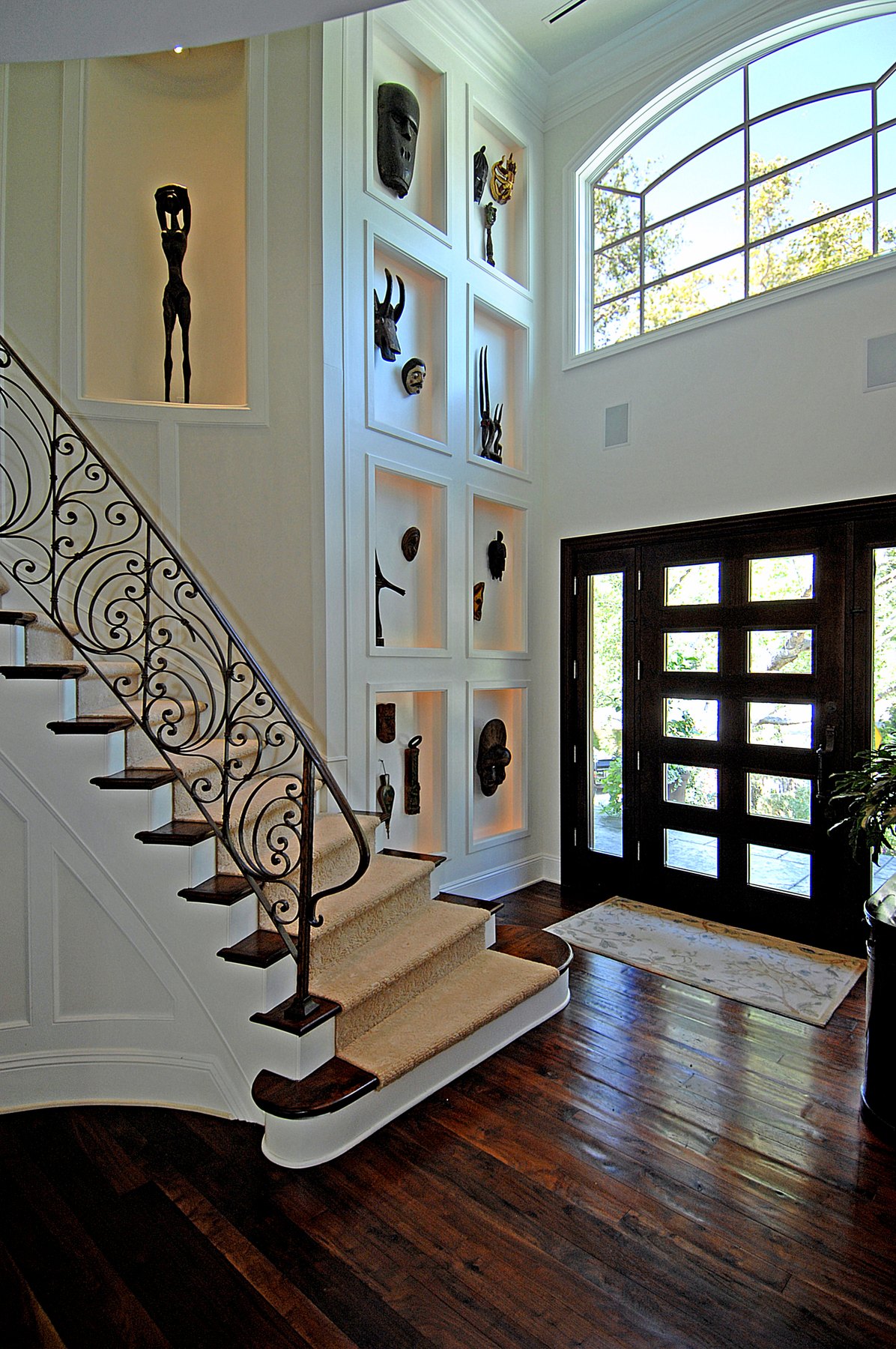 Entry with a wrought-iron stair, art niches and a glazed front door beneath an arched window