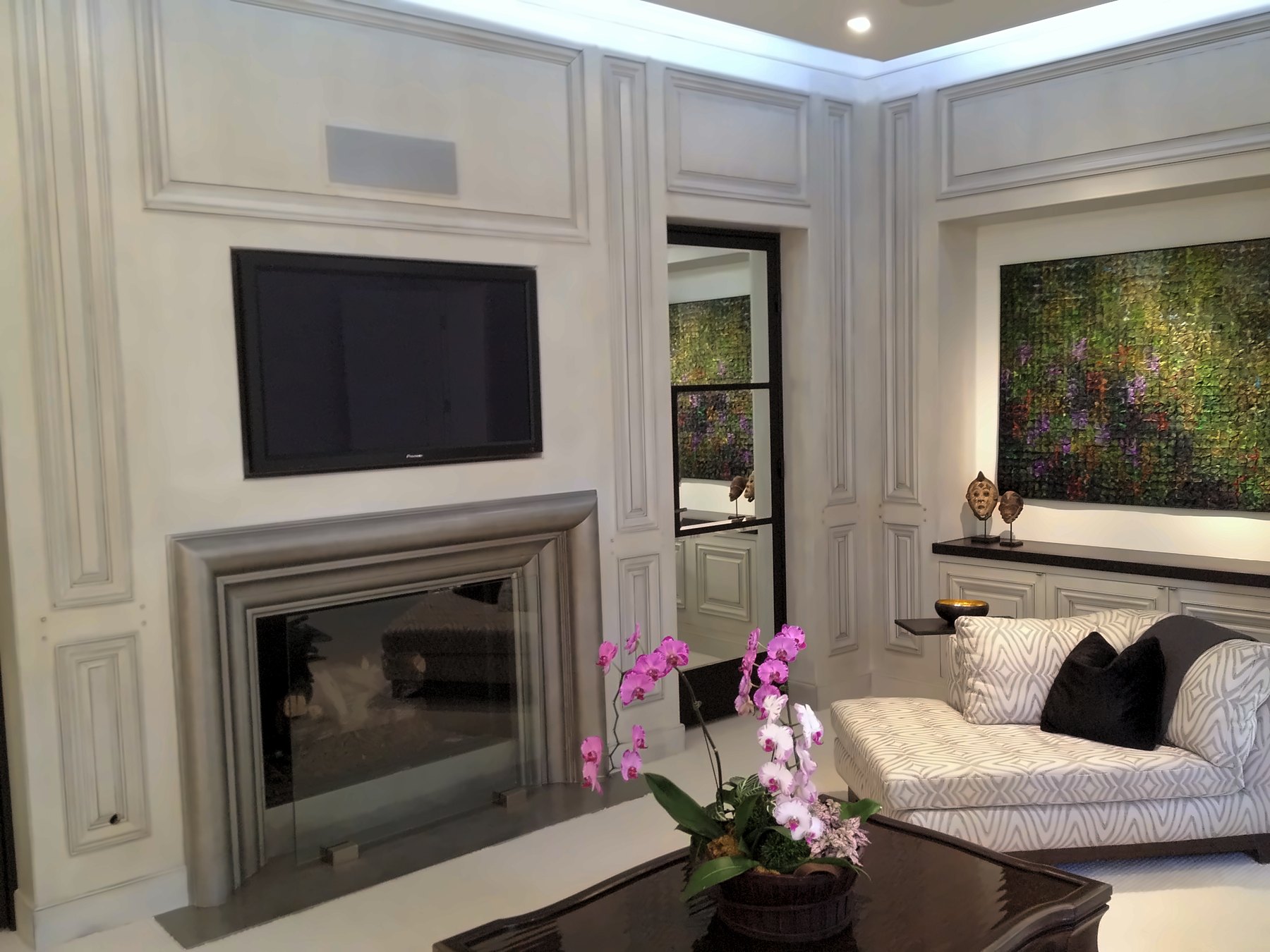 Paneled sitting room with a fireplace, a chaise and orchids