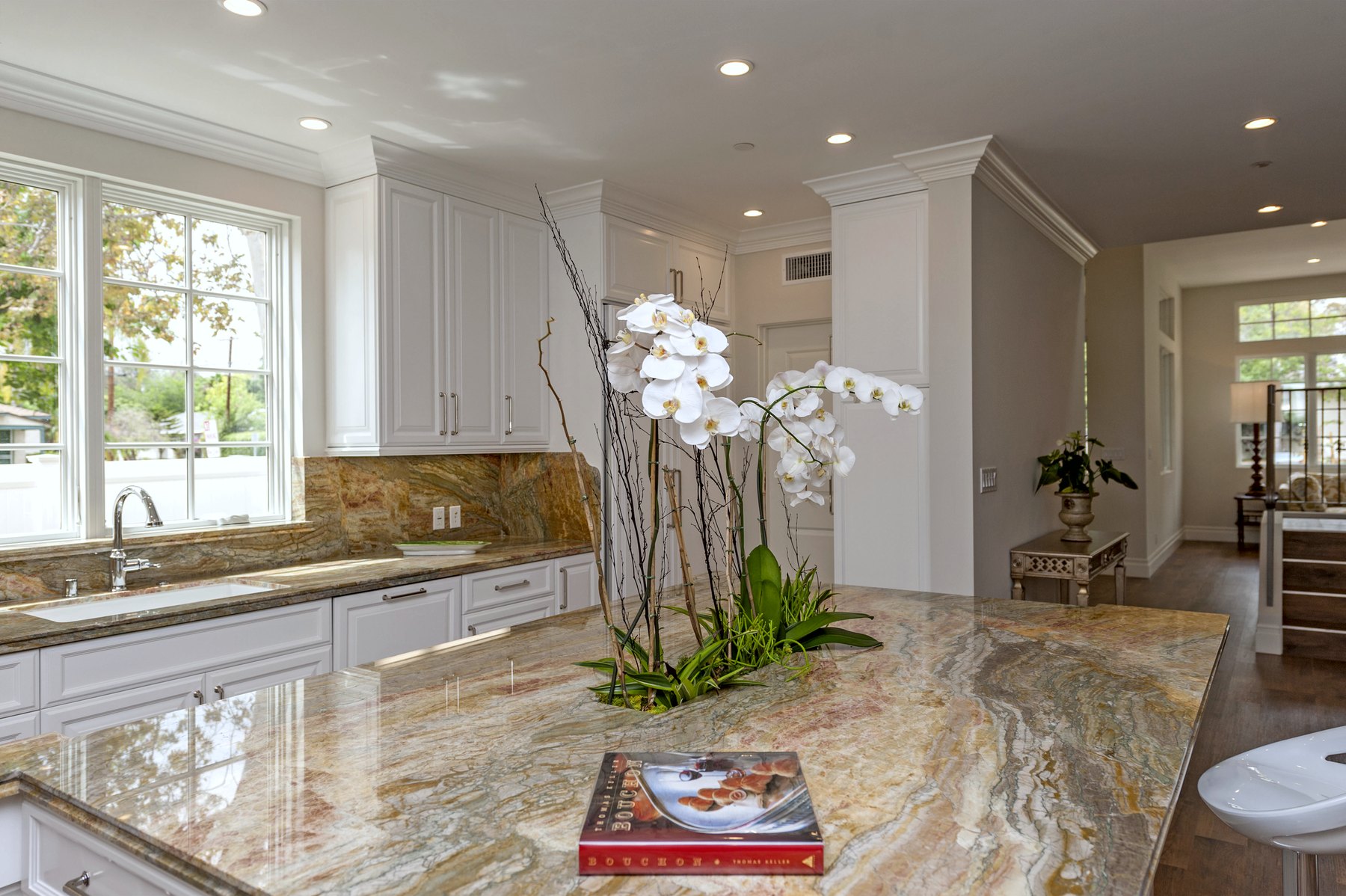 Kitchen island in veined stone with white cabinetry and an orchid