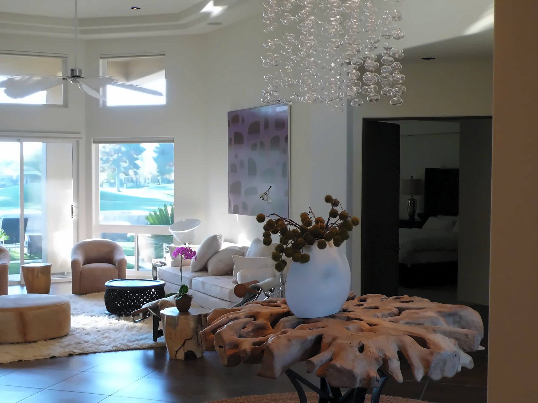 Living room with a sculptural root table, a bubble chandelier and windows to the garden