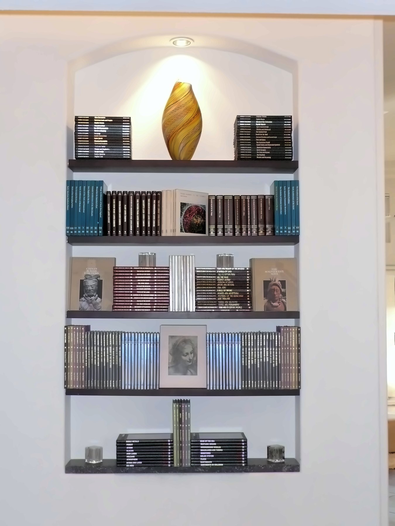 A lit arched niche of books and a glass vase
