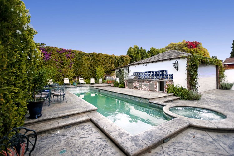 Pool and spa beside a white pool house with a tiled outdoor kitchen