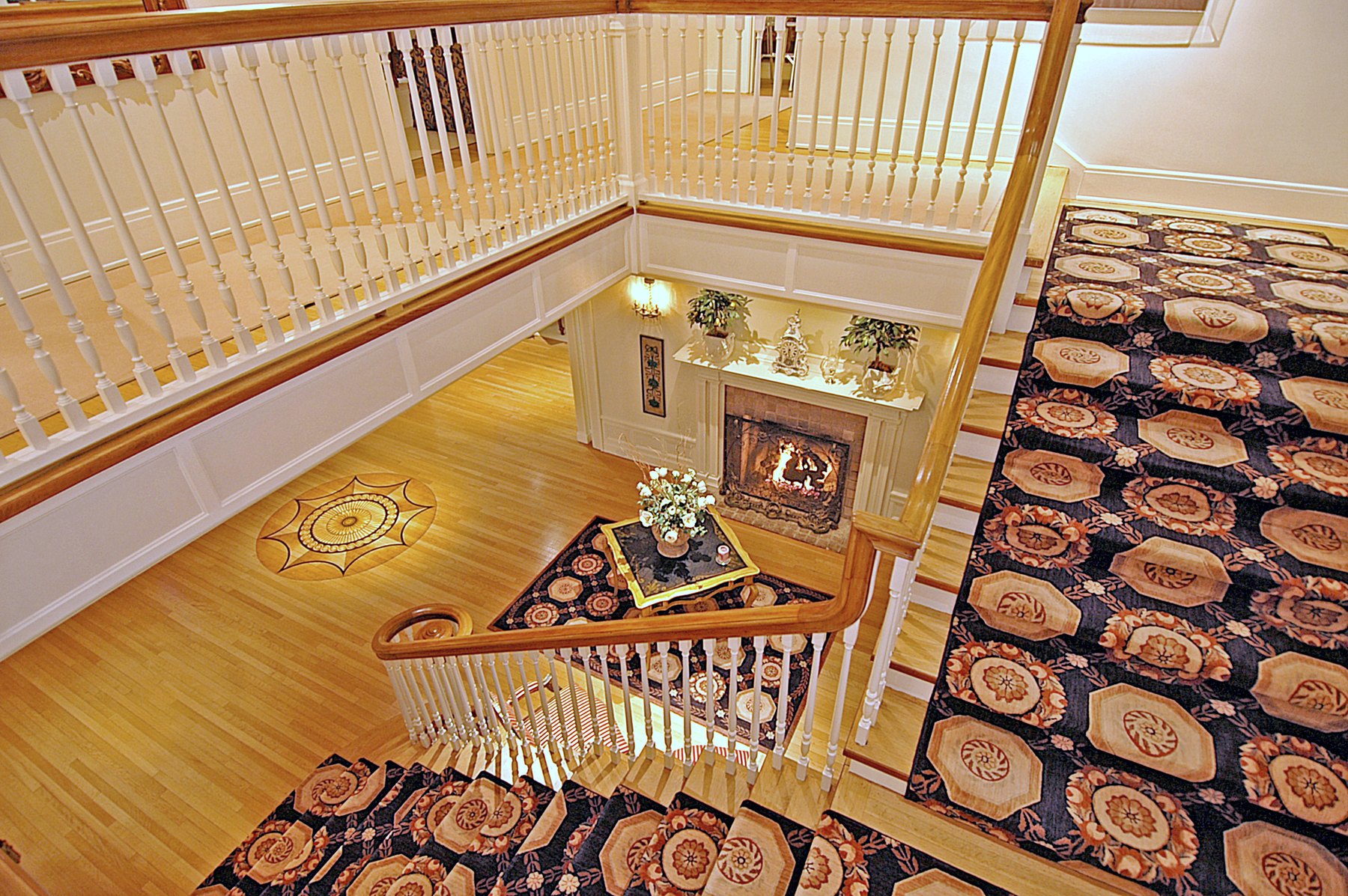 Looking down a stairwell onto a patterned runner and a polished wood floor