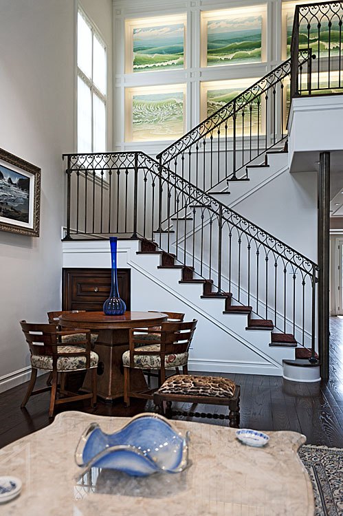 Iron stair rising above a dining table beneath tall windows