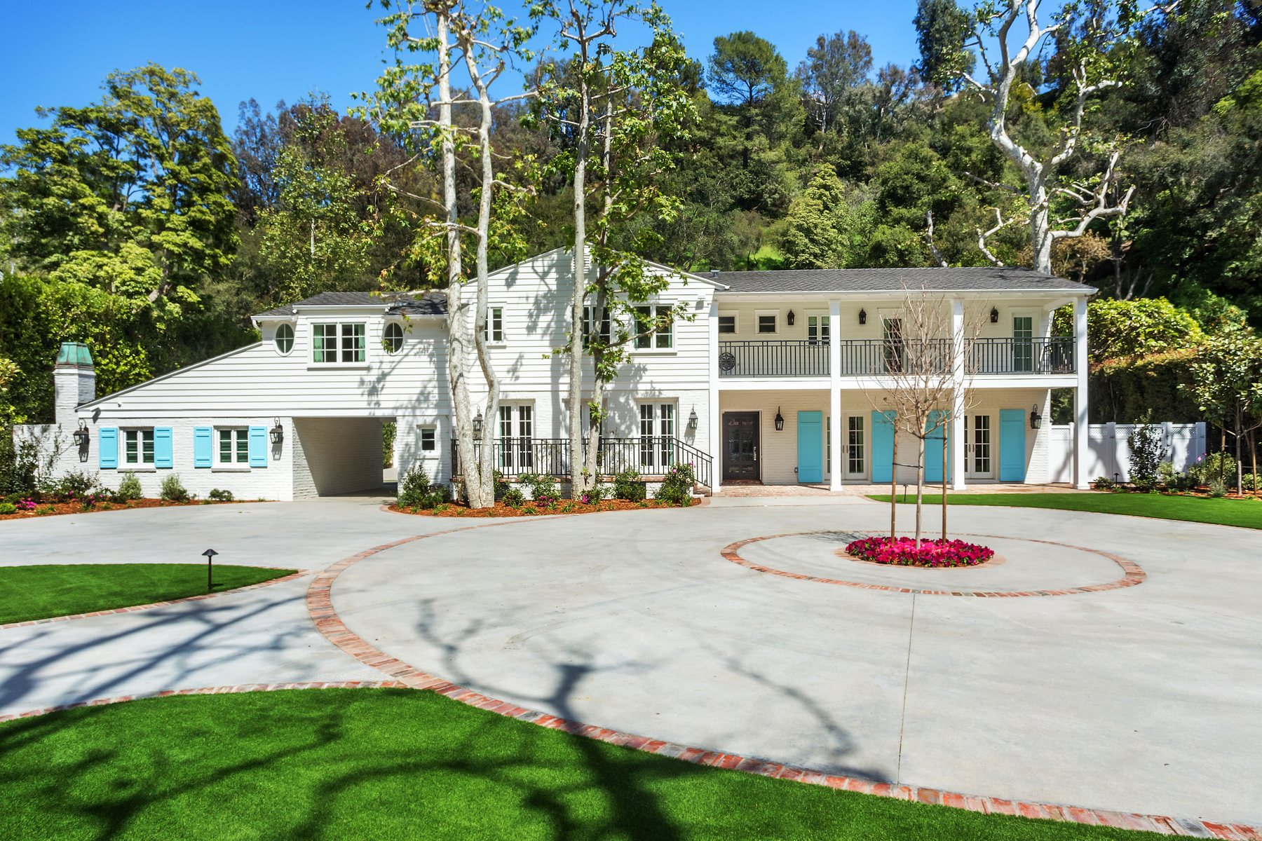 Stone Canyon Residence: the white two-story house with blue shutters behind a circular motor court and sycamores